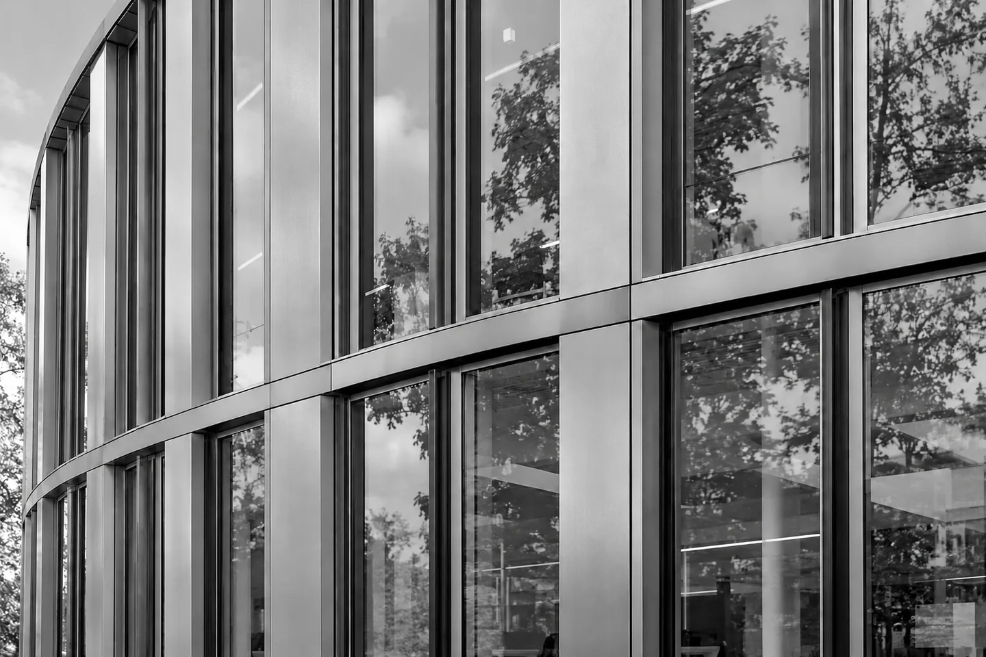 Geschwungene Metallfassade mit Baumreflexionen in den Fenstern